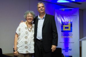 Descrição da imagem. Foto horizontal do senhor Paulo do Eirado ao lado de uma mulher de cabelos grisalhos encaracolados e curtos, lado a lado em pé. Paulo do Eirado está do lado direito e ela do lado esquerdo, ambos no centro da foto. Fim da descrição.