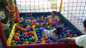 Descrição da imagem. Foto horizontal de uma piscina de bolinhas coloridas com tela de proteção nas laterais e dentro, duas crianças com idade próxima a seis anos. Fim da descrição.